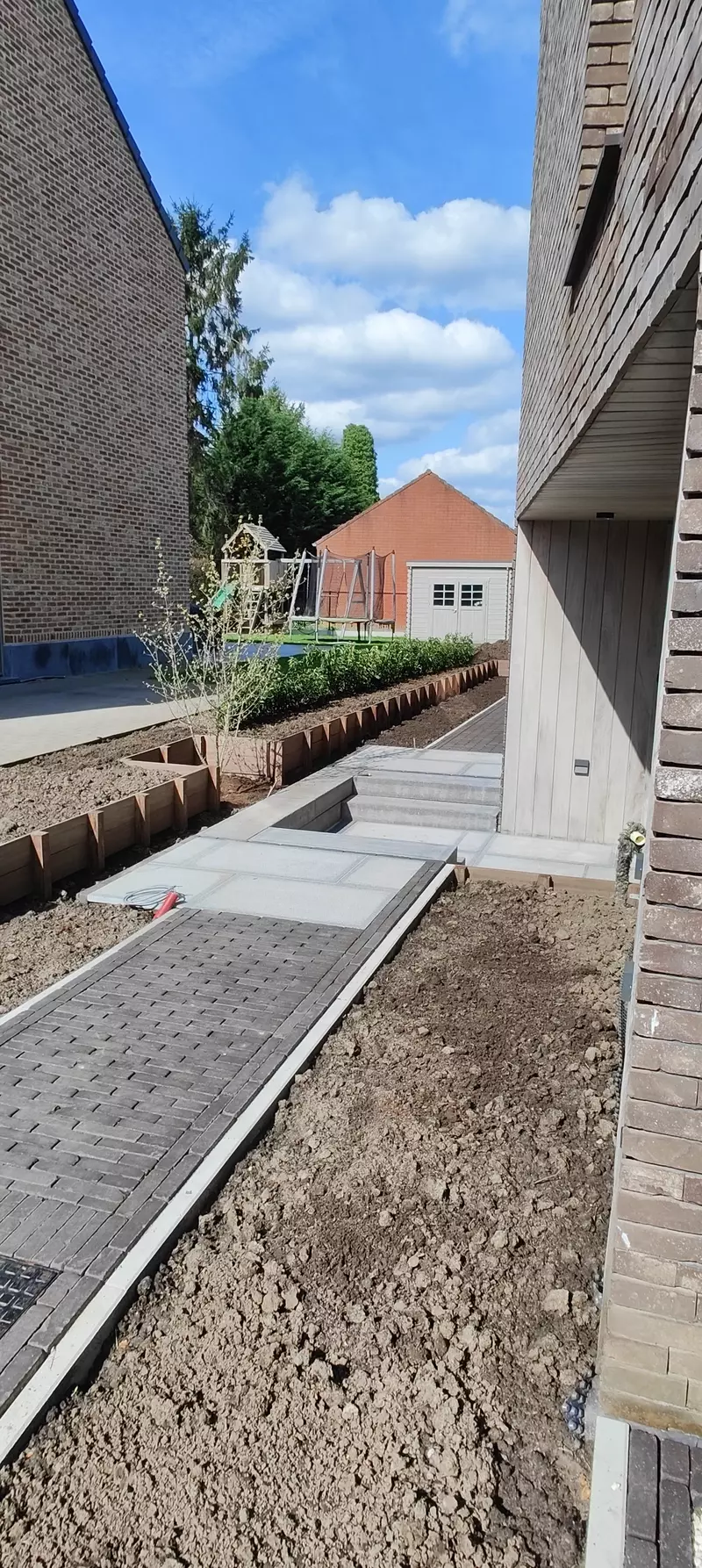 Kleiklinkers met stapstenen en houten keermuur met beplanting
