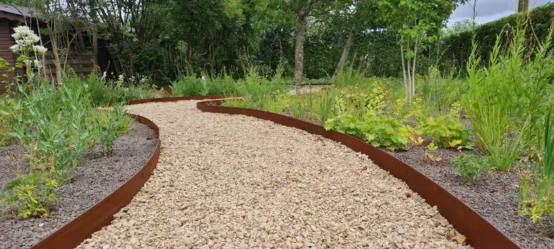 Aanleg tuin met bloeiende planten zodat er gedurende het hele seizoen bloemen zijn. Grindpad met afboordingen in cortenstaal.