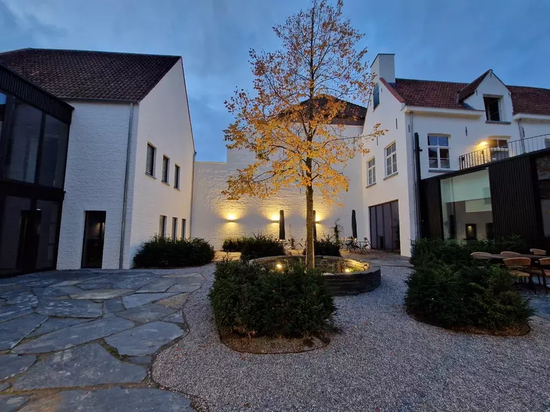Ingesloten stadstuin met waterdoorlatende verharding van flagstones en grind. Klimplanten, groenblijvende taxusmassieven. Volwassen Lindeboom aangeplant