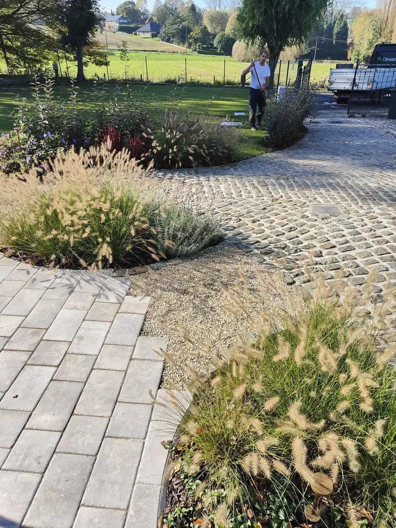 Foto van een bestraat tuinpad met plantvakken en groen uitzicht.