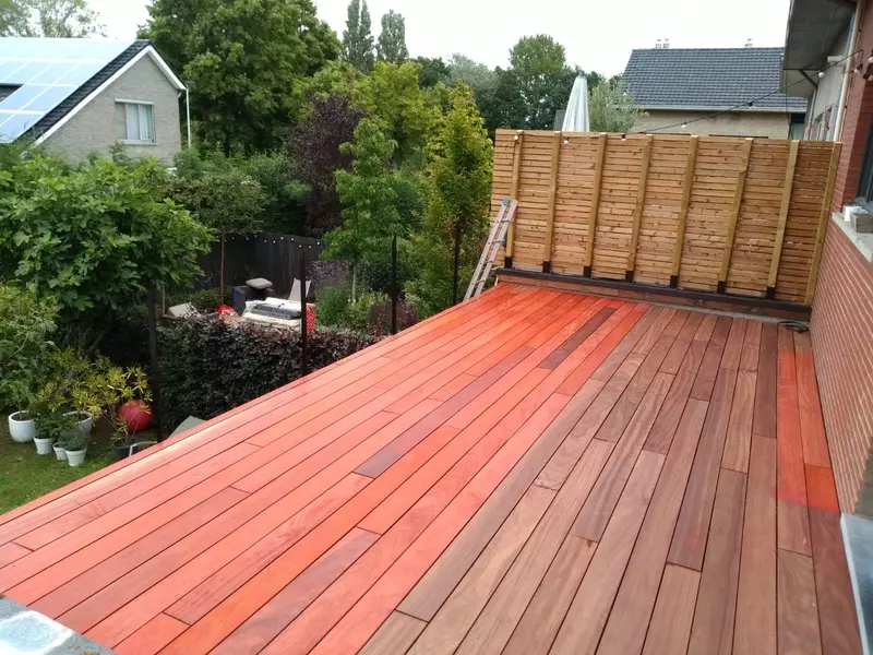 Deze foto toont een terras van nieuw aangelegd terras met warme, houten planken met een houten schutting.