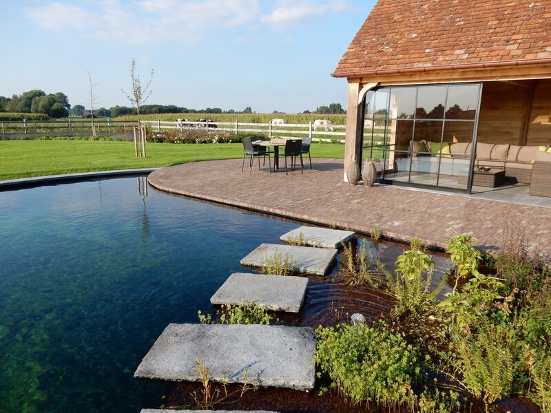 Landelijke tuin met ronde zwemvijver en ruwe blauwsteentegels met een stijlvol, eiken poolhouse.