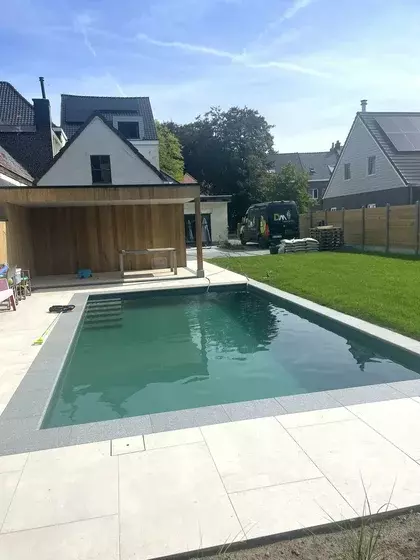 Een strak, modern zwembad dat prachtig contrasteert met de lichte tegels en frisgroene grasmat.